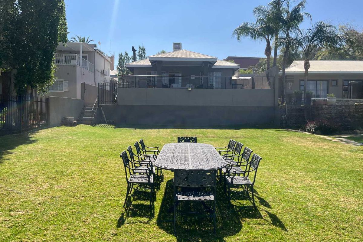 A spacious rear garden featuring a well-maintained lawn, perimeter fencing, and a raised patio area attached to the main house structure.