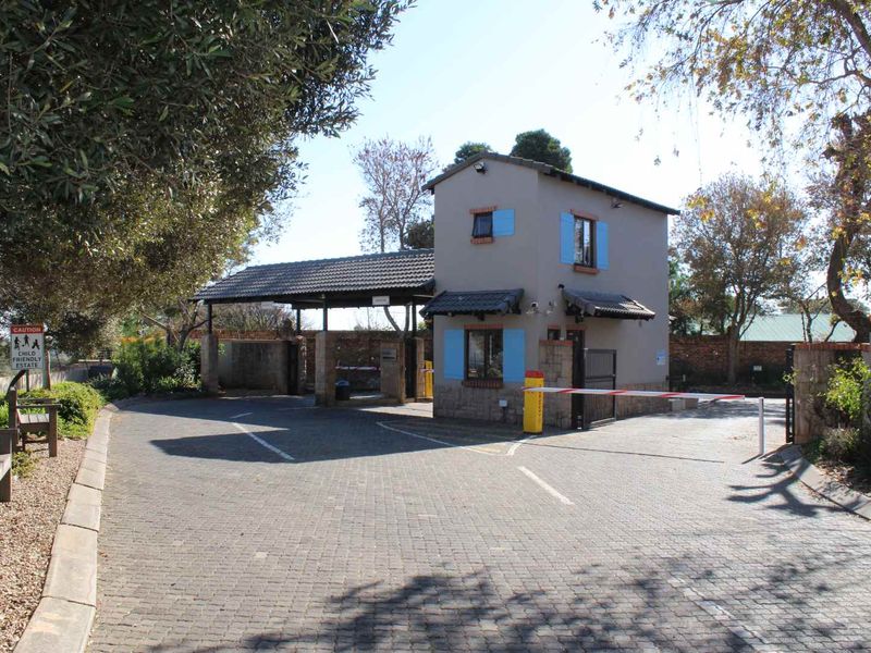 A secure gated entrance to the estate featuring a guardhouse, boom gate access control, and paved driveway.