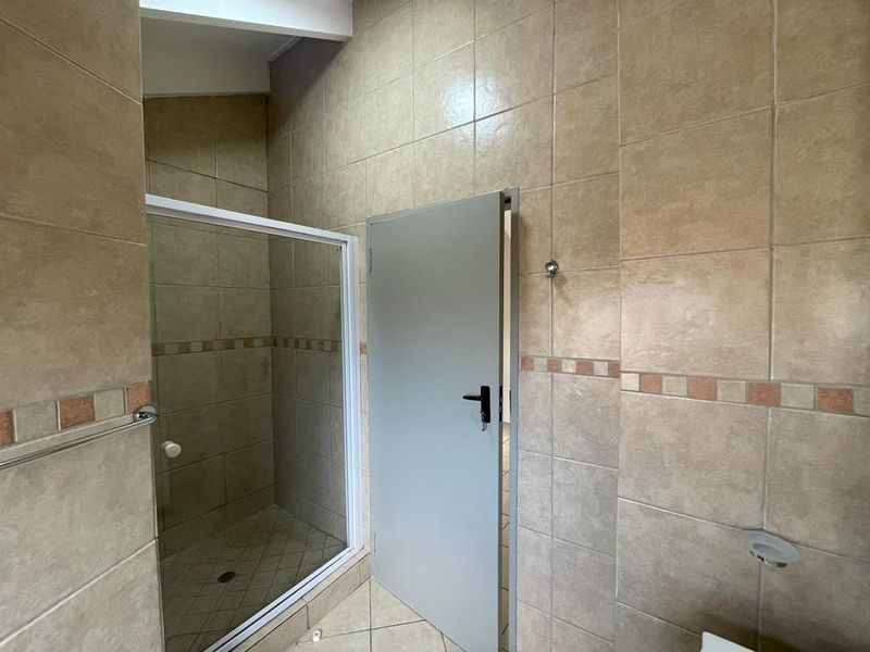 A functional bathroom featuring a shower enclosure with glass door, fully tiled walls, and tiled flooring.