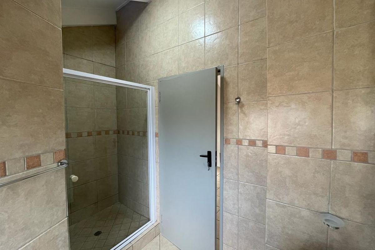 A functional bathroom featuring a shower enclosure with glass door, fully tiled walls, and tiled flooring.