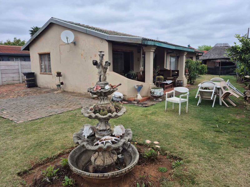 Rear view of the house featuring a covered patio, paved area, and a central stone fountain in the garden.