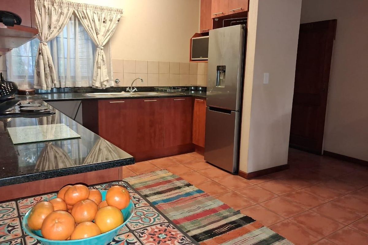 A functional kitchen featuring dark wood cabinetry, granite countertops, tiled backsplash, and integrated sink, with terracotta-style floor tiles.