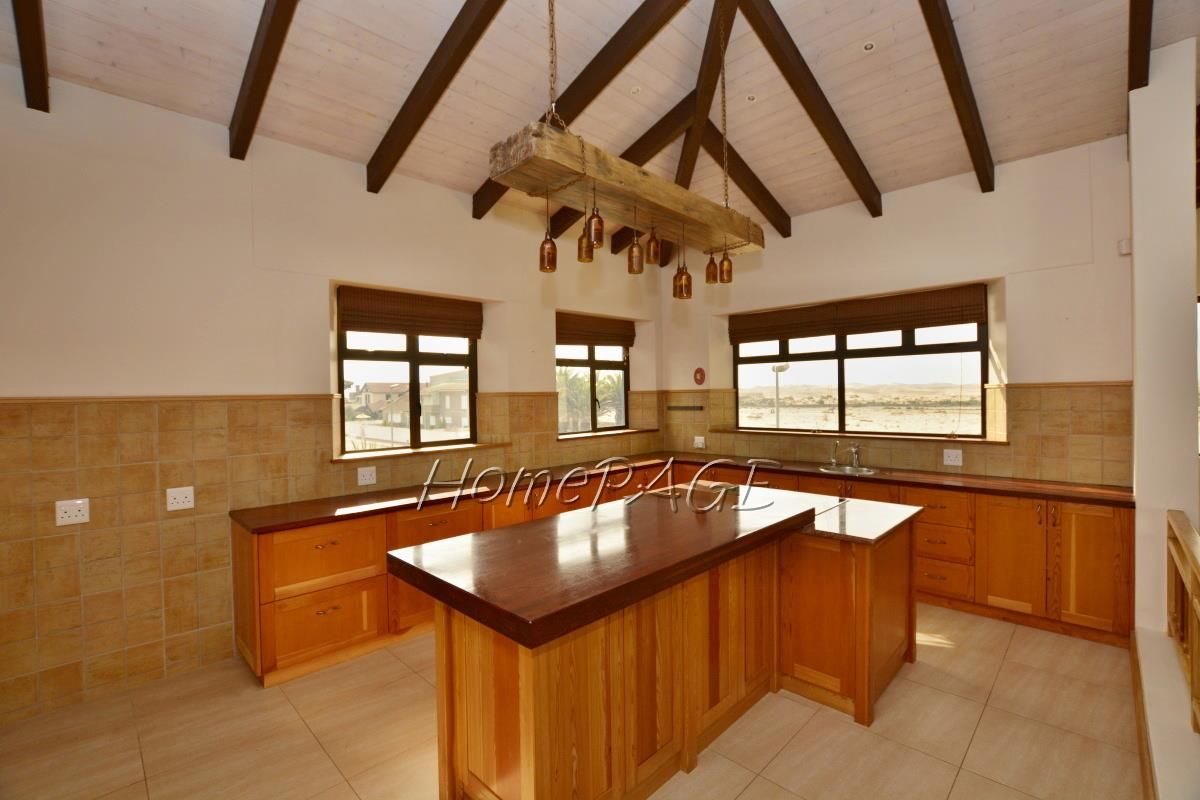 Spacious kitchen featuring timber cabinetry, a central island with a dark wood countertop, tiled splashbacks, and a vaulted ceiling with exposed timber beams.