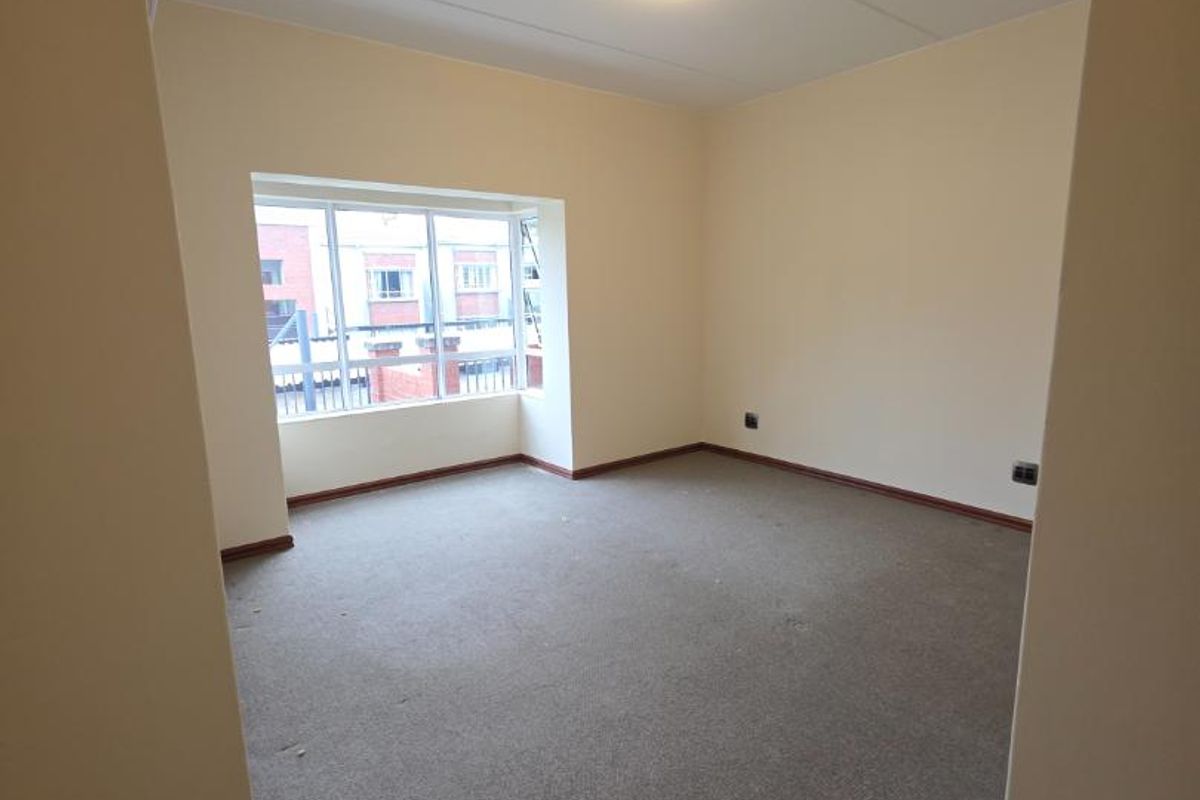 An empty bedroom featuring carpeted flooring, a central ceiling light, and a large window providing natural light.