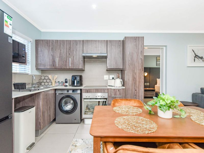 Modern open-plan kitchen featuring wood-grain cabinetry, integrated appliances, and tiled flooring, seamlessly flowing into the adjacent living and dining area.