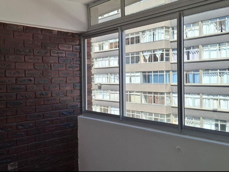 An enclosed balcony area featuring a prominent dark brick feature wall and large sliding windows overlooking the neighboring apartment building.