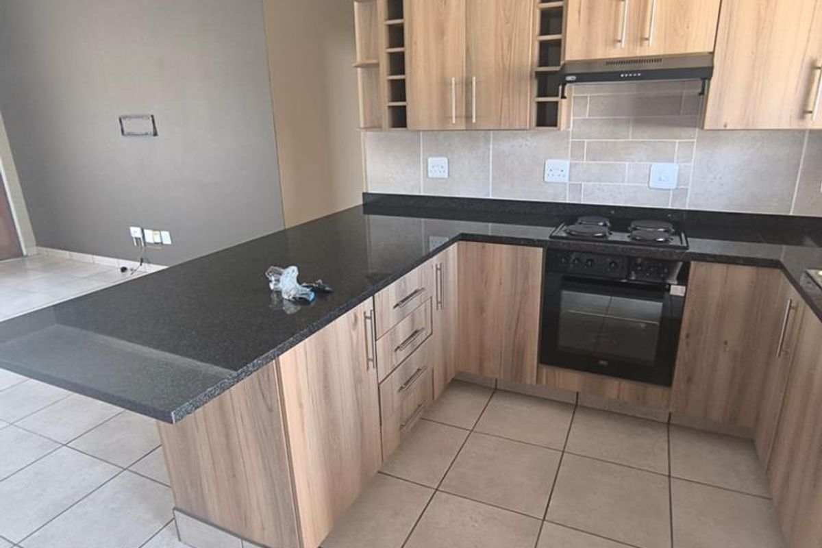 Modern kitchen featuring light wood cabinetry, dark granite countertops, a built-in oven, and a gas hob, seamlessly flowing into an open-plan living area.