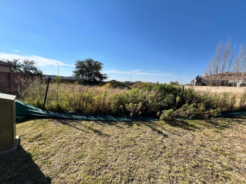 A vacant residential plot featuring a boundary wall, utility box, and significant overgrown vegetation requiring clearing.