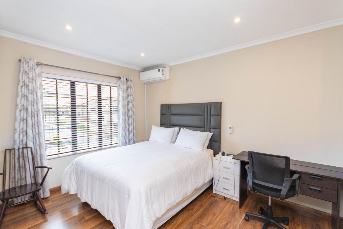 A well-maintained bedroom featuring laminate flooring, recessed downlighting, and a wall-mounted split-system air conditioning unit.