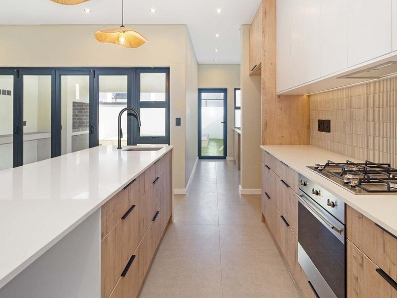 Modern kitchen featuring a large island with quartz countertops, built-in gas hob, oven, and sleek cabinetry, leading to an outdoor patio area.