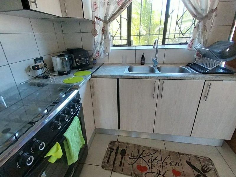 A functional kitchen featuring light-toned cabinetry, laminate countertops, a double sink, and a freestanding stove with a tiled splashback.