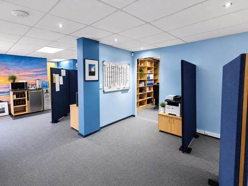 A functional office space featuring a suspended ceiling, recessed lighting, carpeted flooring, and integrated shelving units for organized storage.