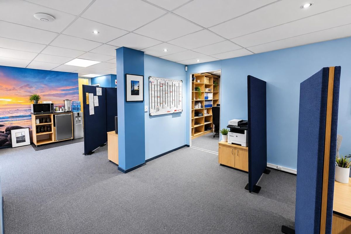 A functional office space featuring a suspended ceiling, recessed lighting, carpeted flooring, and integrated shelving units for organized storage.