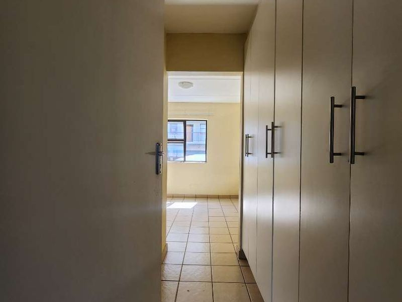 A functional hallway featuring extensive built-in cupboard storage and tiled flooring, leading towards an adjacent room with natural light.