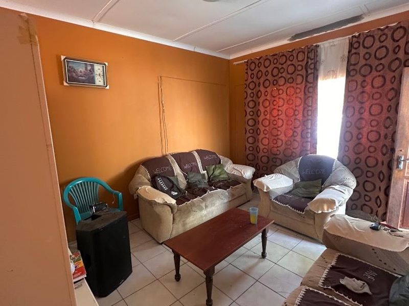 A living room featuring tiled flooring and orange walls, currently showing signs of wear and requiring cosmetic updates to improve the space.