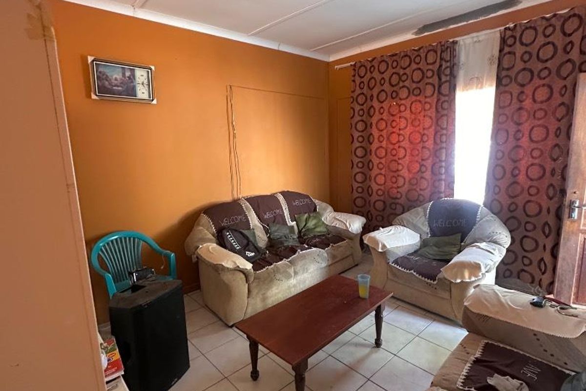 A living room featuring tiled flooring and orange walls, currently showing signs of wear and requiring cosmetic updates to improve the space.