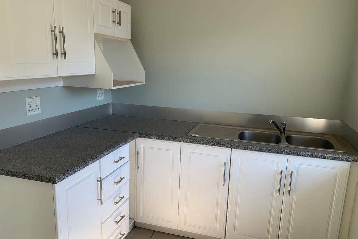 A functional kitchenette featuring white cabinetry, dark granite-look countertops, a stainless steel double sink, and a stainless steel splashback.