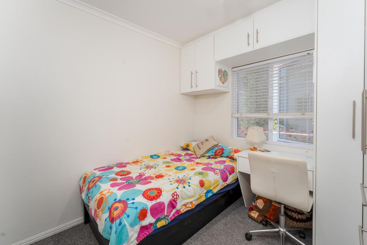 A compact bedroom featuring built-in cupboards, overhead storage cabinets, and a window with venetian blinds.