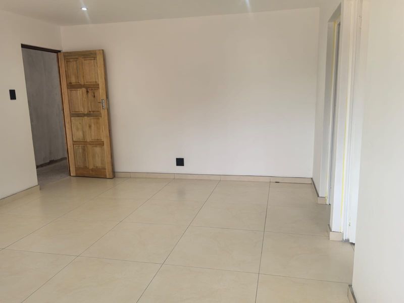 An empty, neutral-toned living area featuring large format floor tiles, recessed lighting, and a solid wood door, ready for personalization.