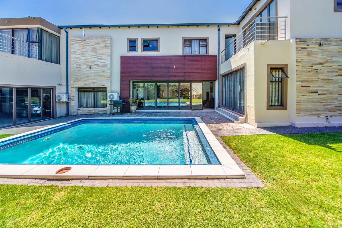 A well-maintained rear exterior view featuring a swimming pool, paved patio area, and modern architectural facade with stone cladding and timber accents.