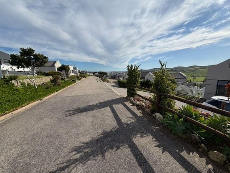 A view looking down a paved residential street within the estate, featuring timber fencing and surrounding cluster homes with distant landscape views.
