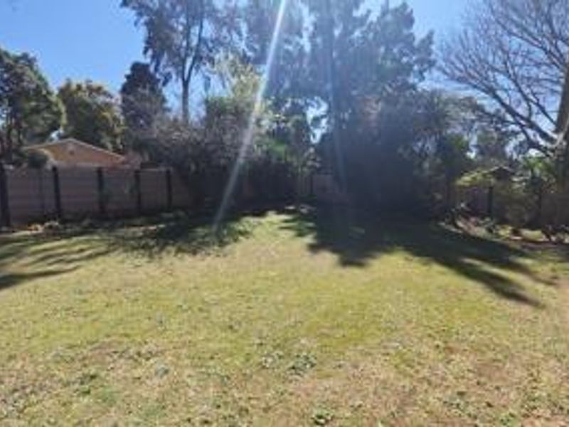 A spacious private backyard featuring a large lawn area enclosed by perimeter walls and mature trees.