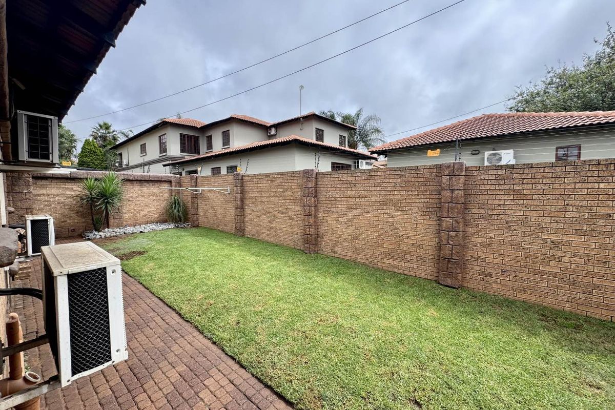 A private rear garden featuring a paved patio area, a well-maintained lawn, and secure brick boundary walls with electric fencing.