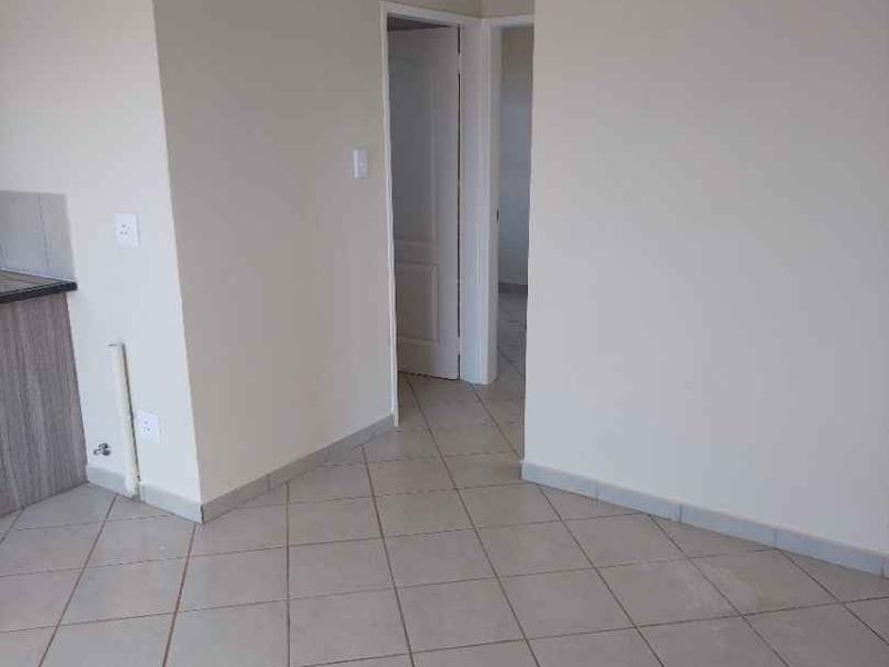 An empty open-plan living area featuring neutral tiled flooring, coved cornicing, and access to adjacent rooms.