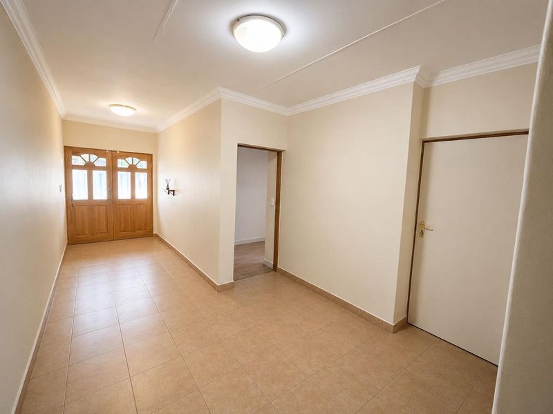 A spacious and well-maintained entrance hall featuring neutral tiled flooring, classic ceiling cornices, and a solid wooden double front door.