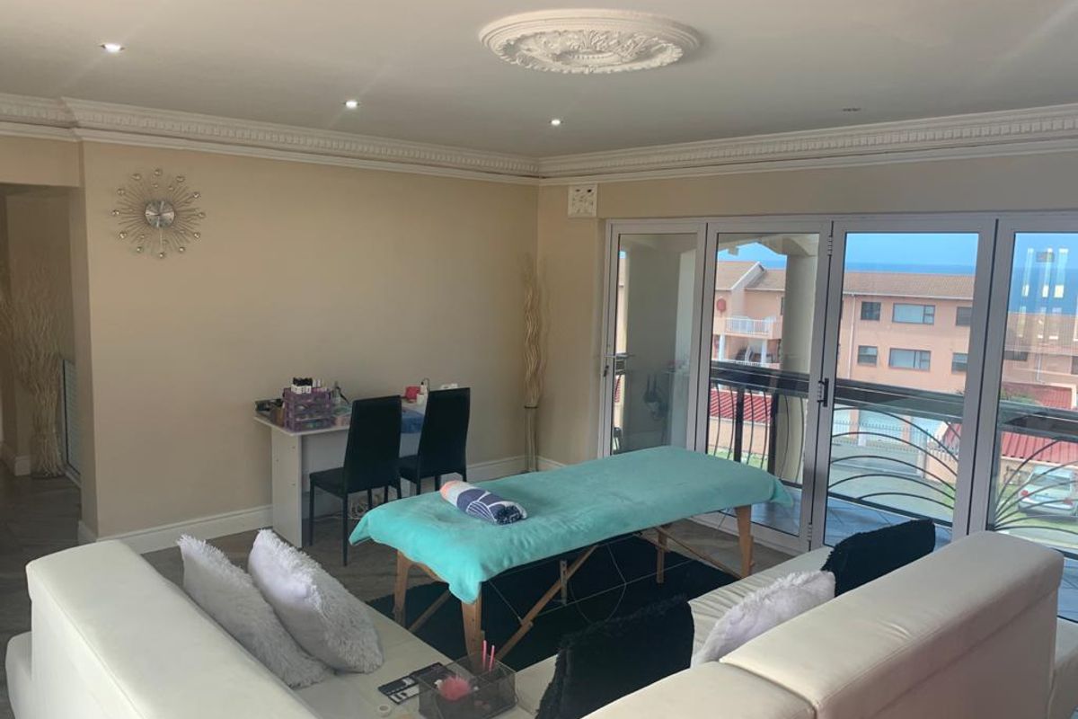 Spacious living area featuring decorative crown molding, ceiling rose, recessed lighting, and large sliding glass doors providing access to a balcony with coastal views.