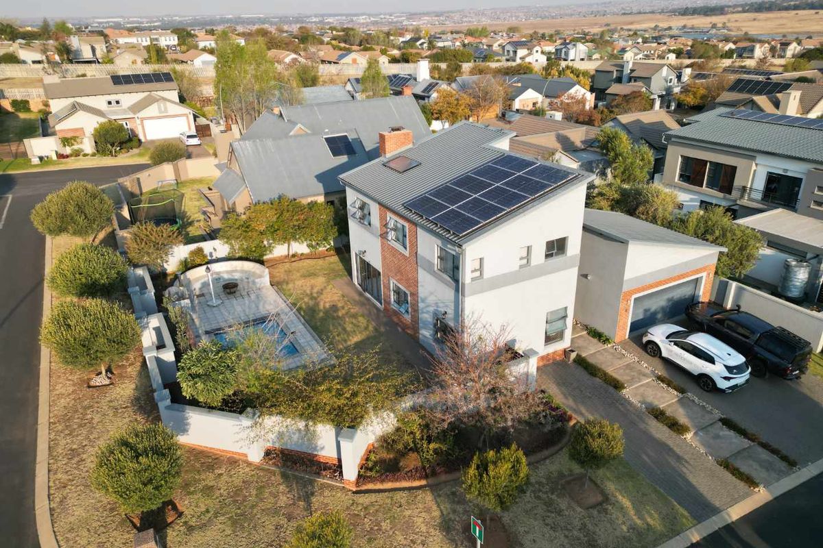 Aerial view of a two-story residential property featuring a swimming pool, landscaped garden, solar panels, and an attached garage in a suburban estate.