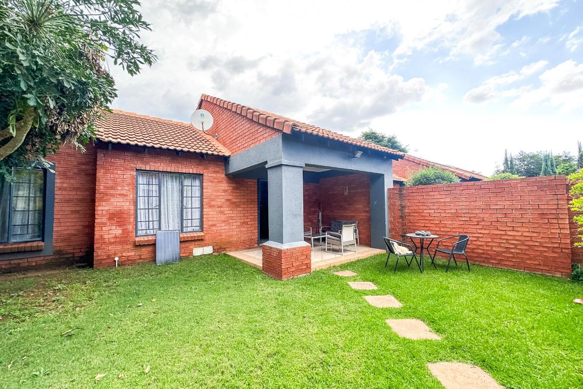 Rear view of the townhouse featuring a covered patio, brick exterior walls, tiled roof, and a private garden with stone pathway.
