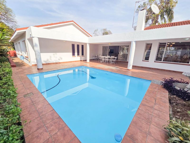 A well-maintained outdoor pool area featuring a tiled patio, covered veranda, and a swimming pool, ideal for outdoor relaxation and entertainment.