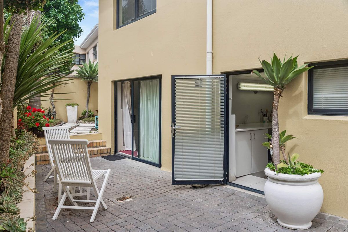 A paved rear patio area featuring sliding glass doors and a secondary access door leading into the home, complemented by landscaped garden beds.