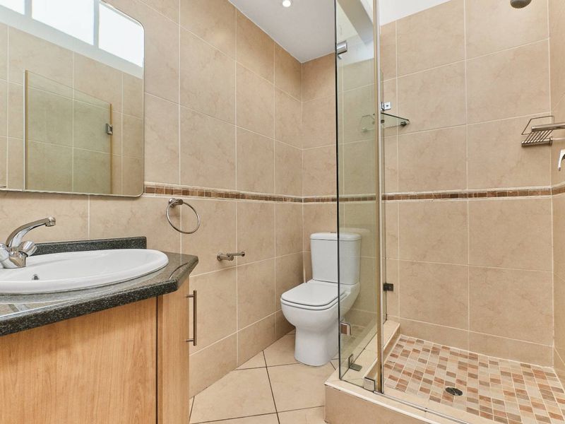 A clean, functional bathroom featuring a vanity with granite countertop, a glass-enclosed shower, and neutral wall tiling throughout.
