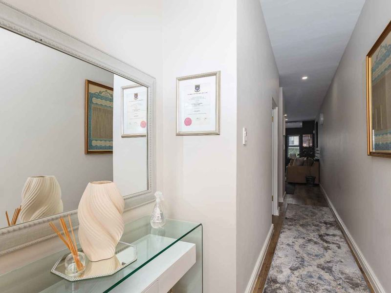 A well-lit hallway featuring neutral wall tones, recessed downlighting, and durable laminate flooring, providing a clean transition between living spaces.