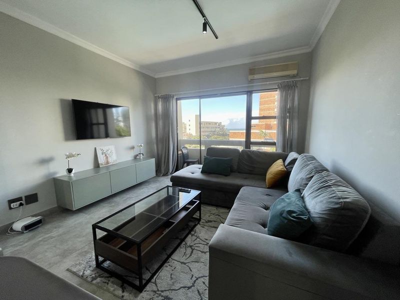 A well-maintained living room featuring a split-system air conditioner, track lighting, and large sliding glass doors providing natural light and exterior views.