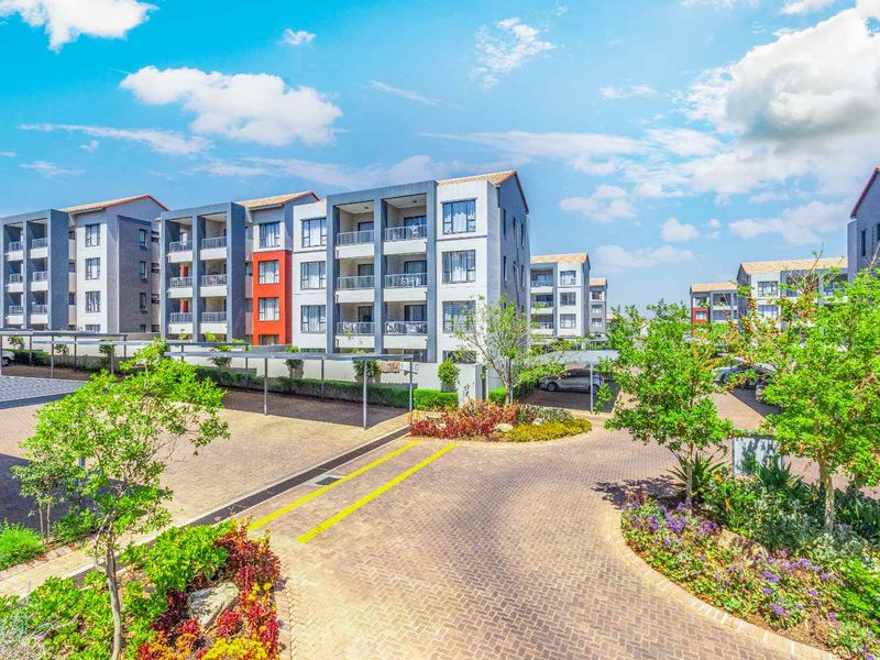 A well-maintained apartment complex featuring paved driveways, covered parking bays, and landscaped gardens with multi-story residential buildings.