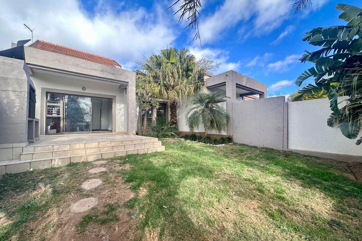 A private rear garden featuring a tiled patio area, established palm trees, and a perimeter boundary wall.