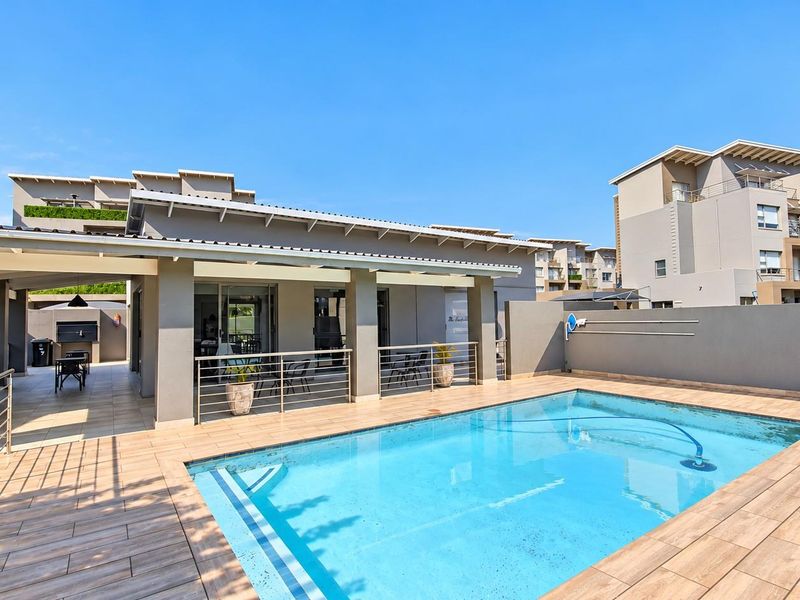 A well-maintained outdoor pool area featuring a tiled deck, covered patio space, and modern stainless steel balustrades, perfect for outdoor relaxation.