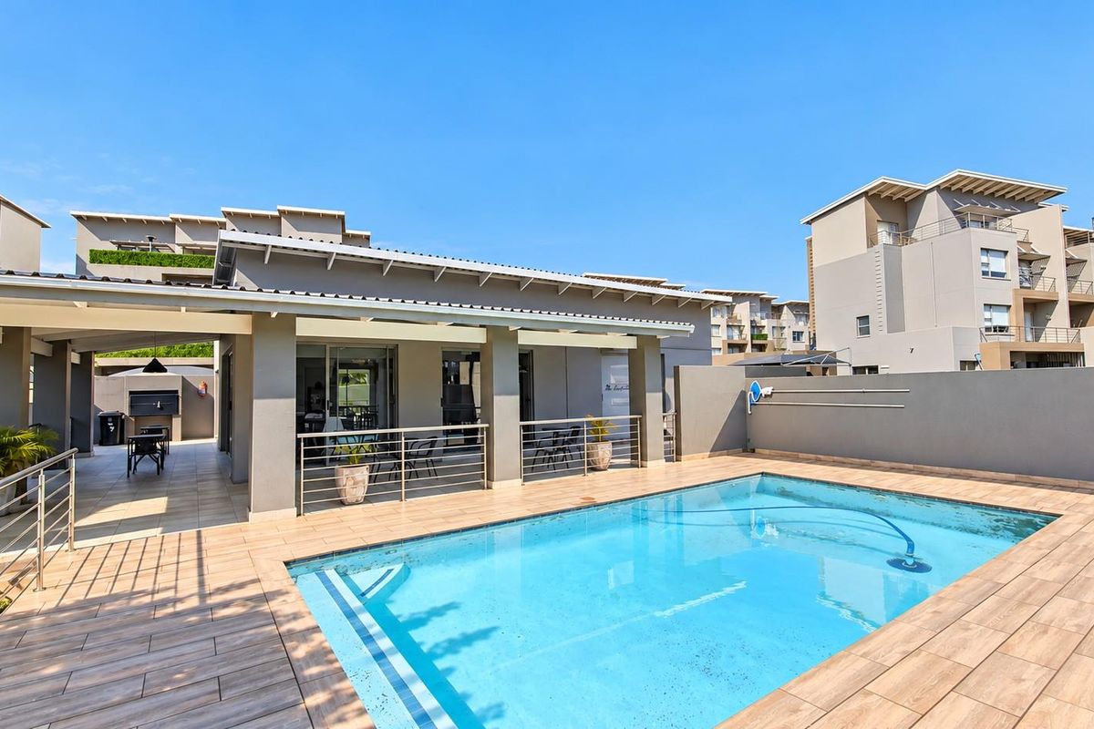 A well-maintained outdoor pool area featuring a tiled deck, covered patio space, and modern stainless steel balustrades, perfect for outdoor relaxation.