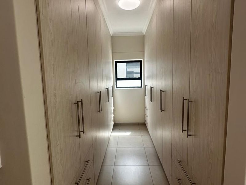 A well-maintained walk-in closet or dressing area featuring extensive built-in cabinetry with light wood finishes and neutral floor tiles.