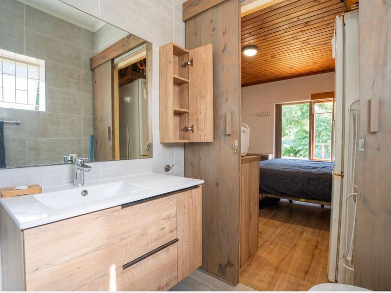Modern bathroom featuring a timber vanity with integrated sink, large mirror, and sliding wooden door leading to an adjacent bedroom with timber ceiling.