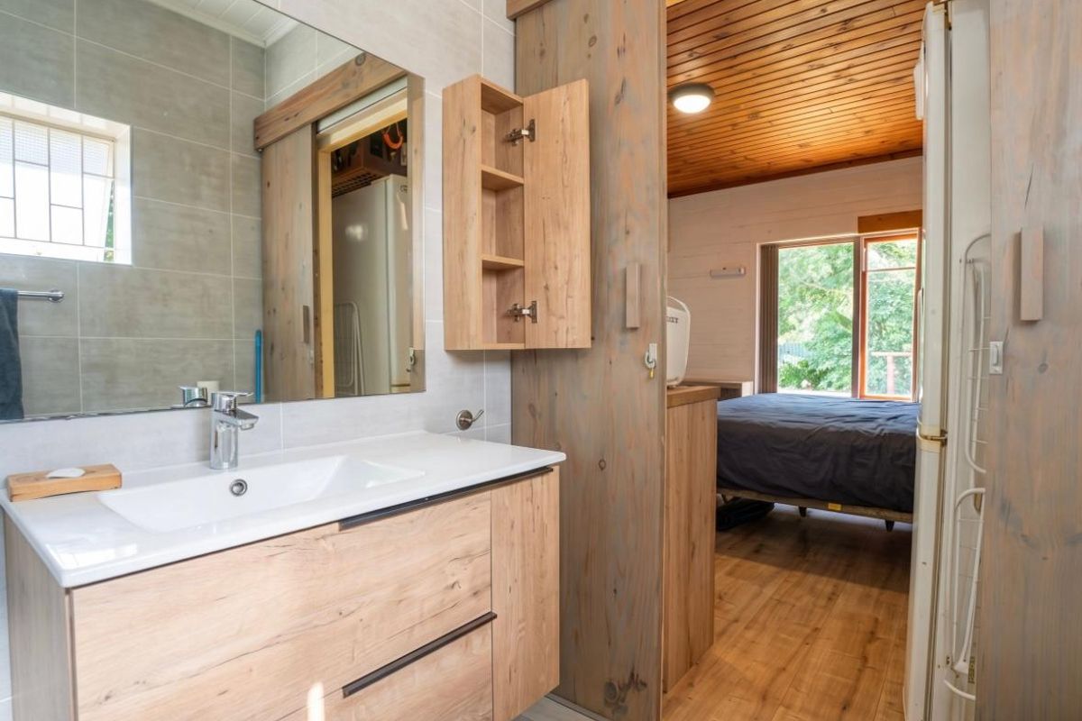 Modern bathroom featuring a timber vanity with integrated sink, large mirror, and sliding wooden door leading to an adjacent bedroom with timber ceiling.