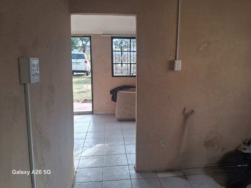 An empty living area featuring tiled flooring, security bars on windows, and visible surface-mounted electrical conduits, requiring cosmetic updates and wall repairs.