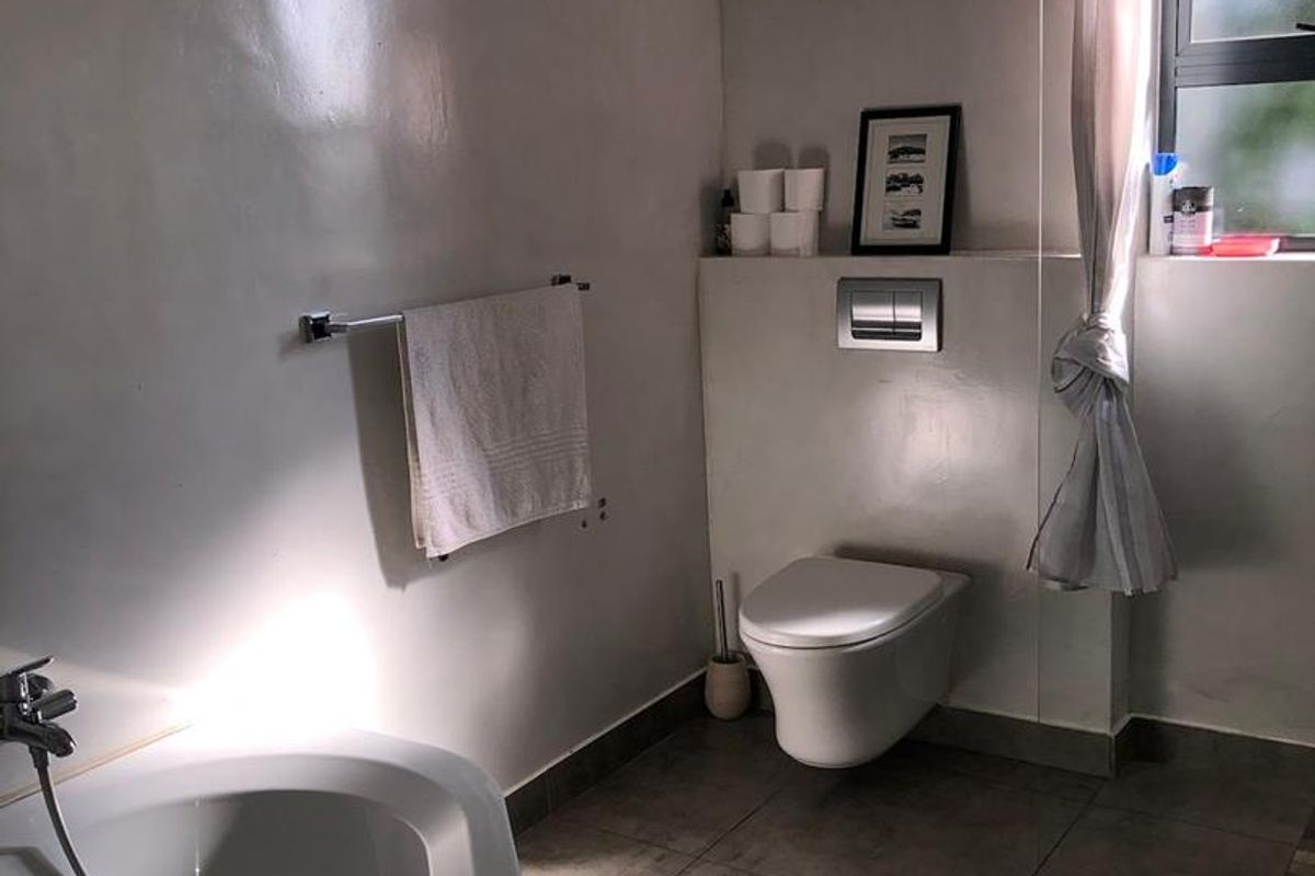 Modern bathroom featuring a wall-mounted toilet, a freestanding bathtub with handheld shower fixture, and tiled flooring.