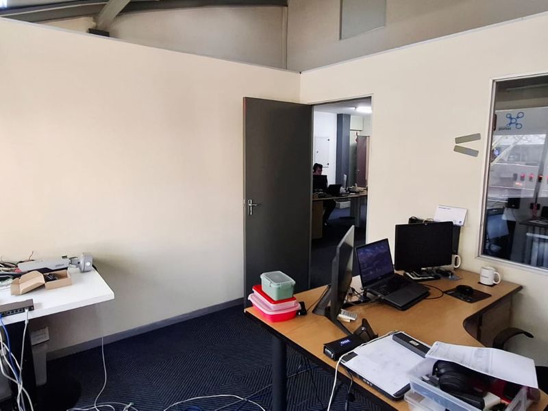 A functional office space featuring carpeted flooring, a glass partition wall, and an internal door leading to an adjacent workspace.