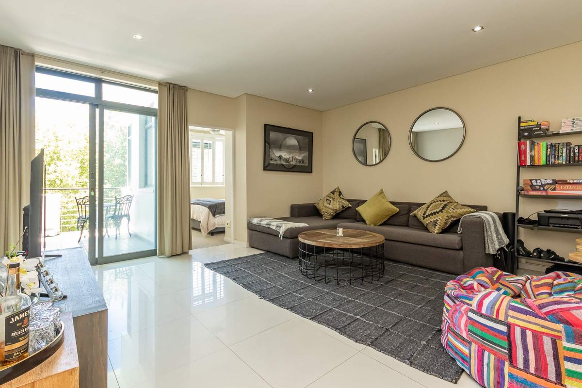 A bright, open-plan living area featuring polished tile flooring, recessed downlighting, and large sliding glass doors leading to a private balcony.