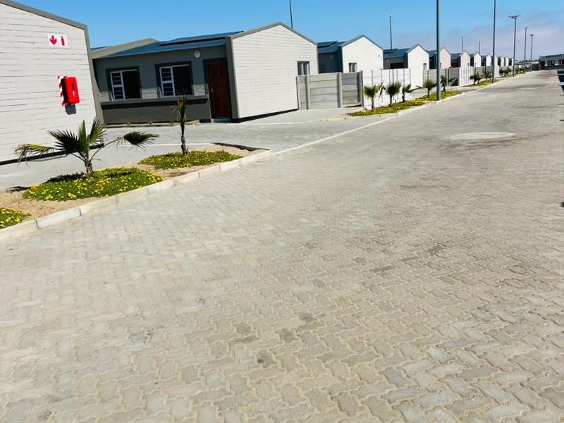 A view of a residential townhouse complex street featuring paved driveways, boundary walls, and modern exterior finishes.