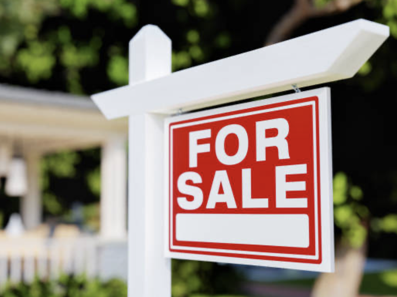 A real estate for sale sign positioned in front of a residential property.